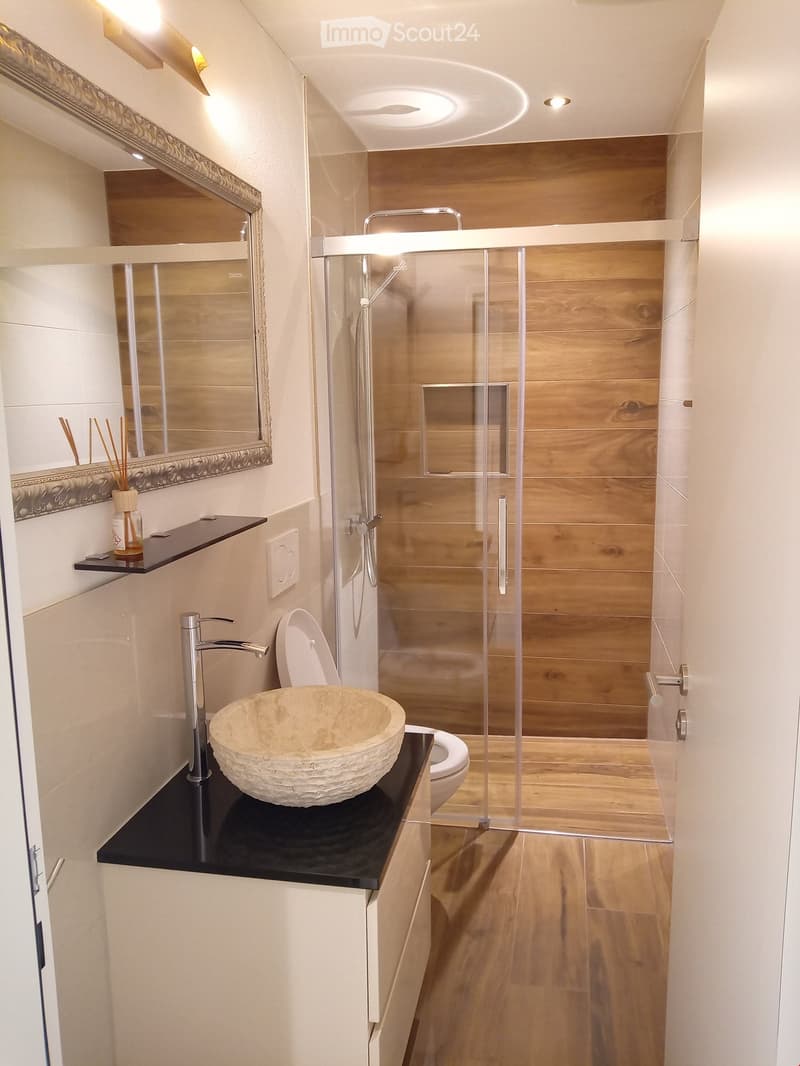 Bathroom with wooden floor, mirror, sink, toilet, shower, wooden wall