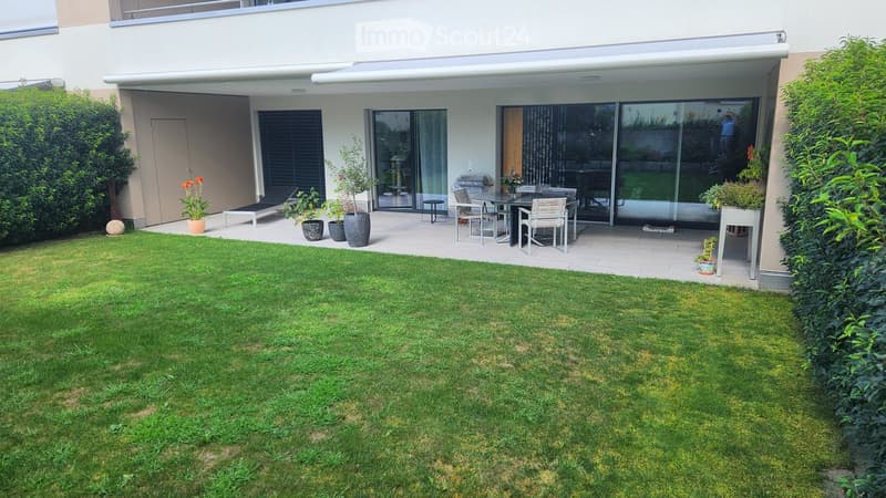 patio with table and chairs, plants, shrubs, green grass