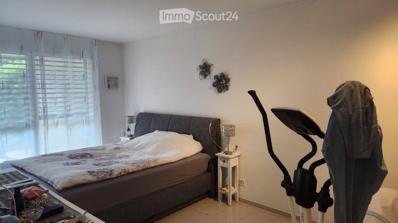 Bedroom with bed, nightstands, lamps, exercise equipment, and a window with curtains