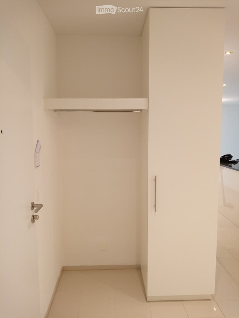 Empty room with white walls, white floor, a door, a wardrobe, and a shelf