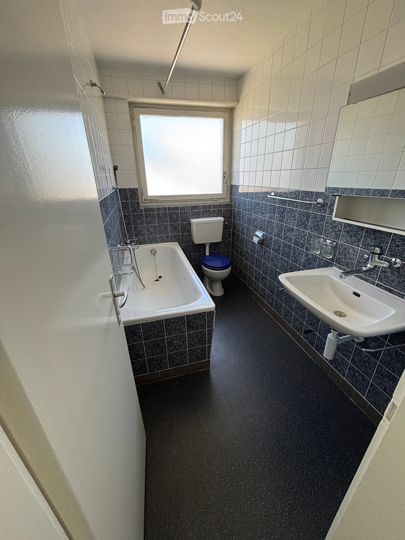 Bathroom with a bathtub, toilet, and sink, featuring tiled walls and a window for natural light.