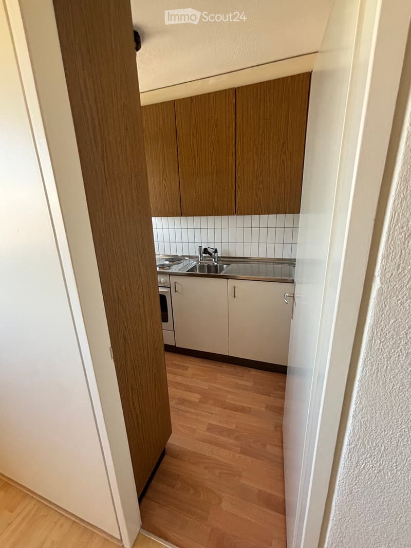 Modern kitchen with wooden cabinets, white tiled backsplash, stainless steel sink, and oven. Light wooden flooring throughout.