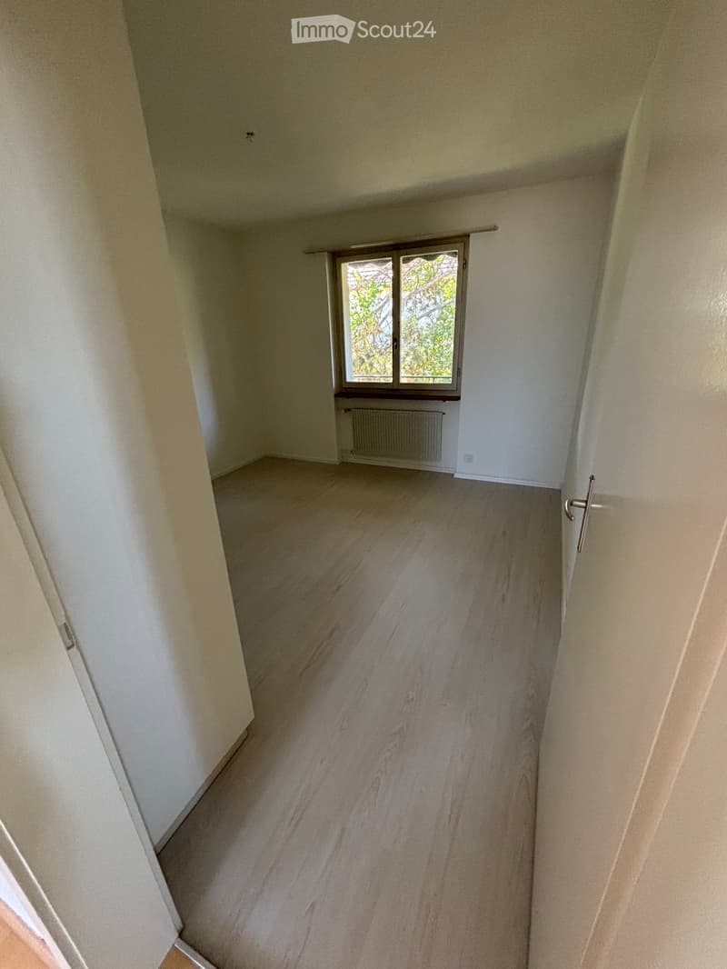 Empty room with light-colored walls, wooden flooring, and a window with a radiator below it.