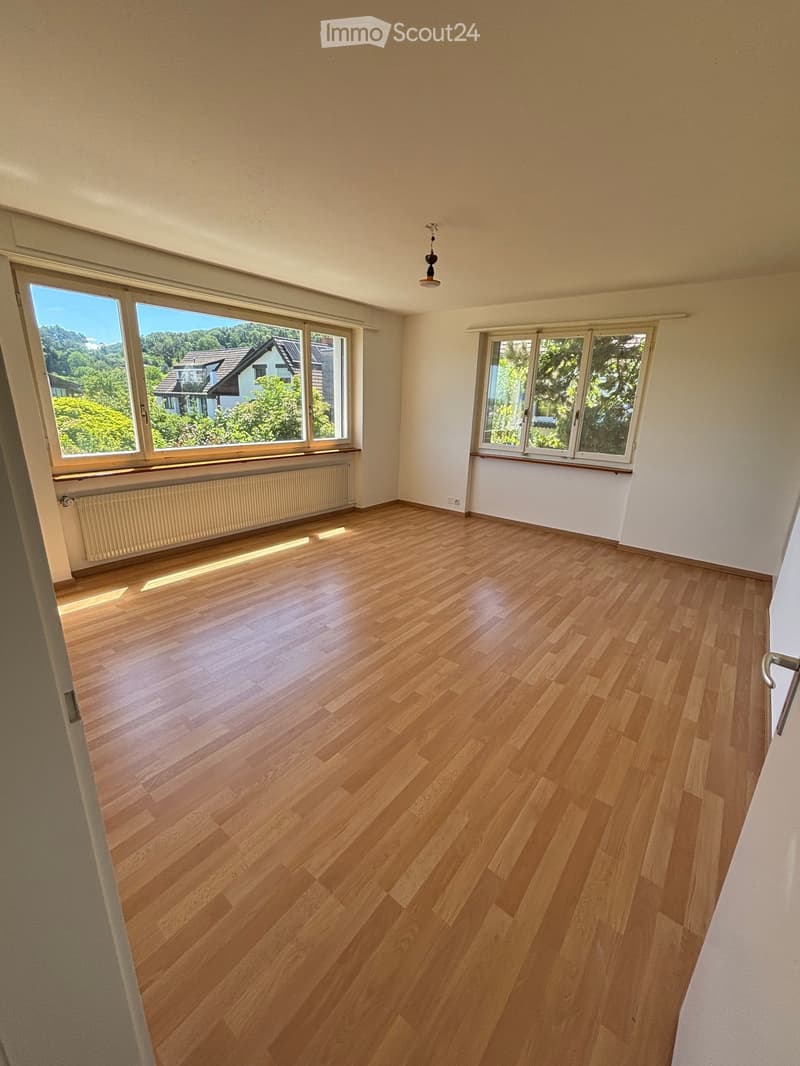 Empty room with wooden flooring, large windows, radiator, and a hanging light fixture.