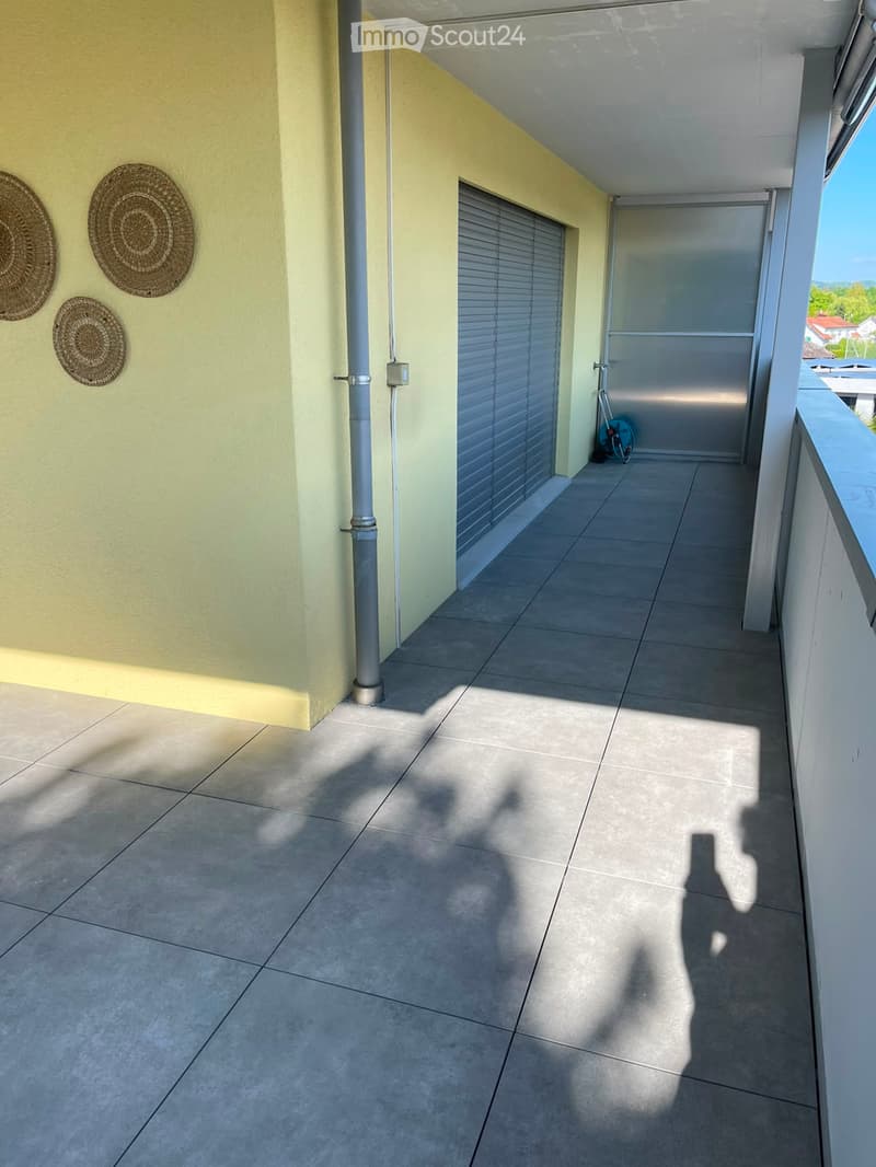 Balcony with tiled floor, light yellow walls, three woven wall hangings, a closed sliding door, and a bicycle leaning against the wall.