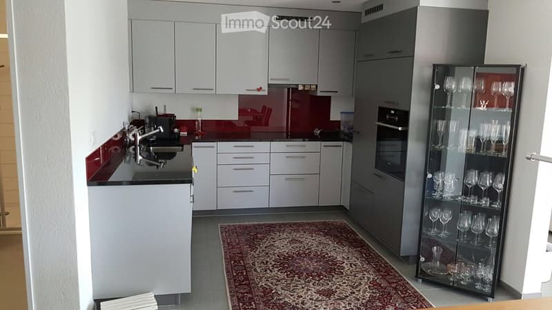 Modern kitchen with white cabinets, stainless steel appliances, a wine rack, and a red accent wall.