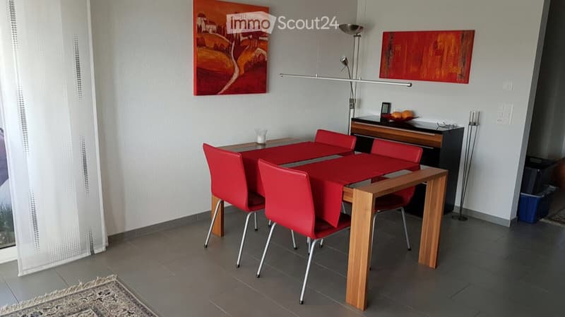Dining room with a modern wooden dining table, red chairs, floor lamp, and two paintings on the wall.