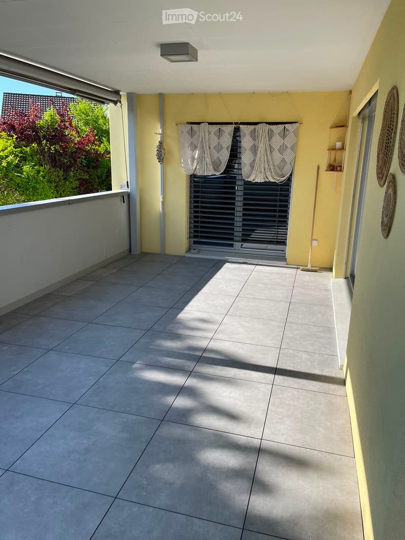 Balcony with tiled floor, yellow walls, white curtains, and a view of greenery outside.