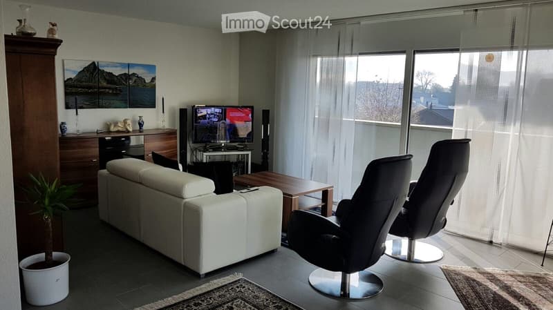 Modern living room with large windows, white sofa, black leather chair, coffee table, TV, decorative vases, and artwork on the wall.