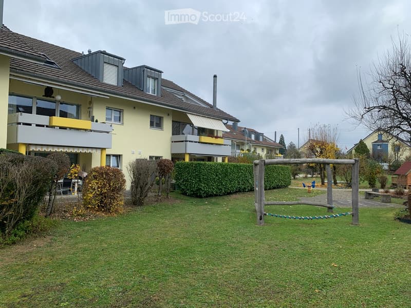 yellow building with brown roof, balconies, hedges, lawn, playground