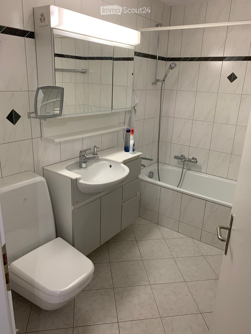 modern bathroom with white tiles, white sink, white toilet, bathtub, shower, mirror, and a shower head