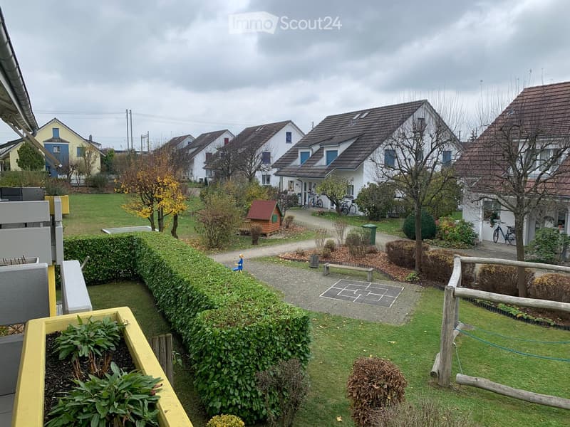 A garden with a small wooden house, a bench, and a small pathway. There are also some plants and trees in the garden.