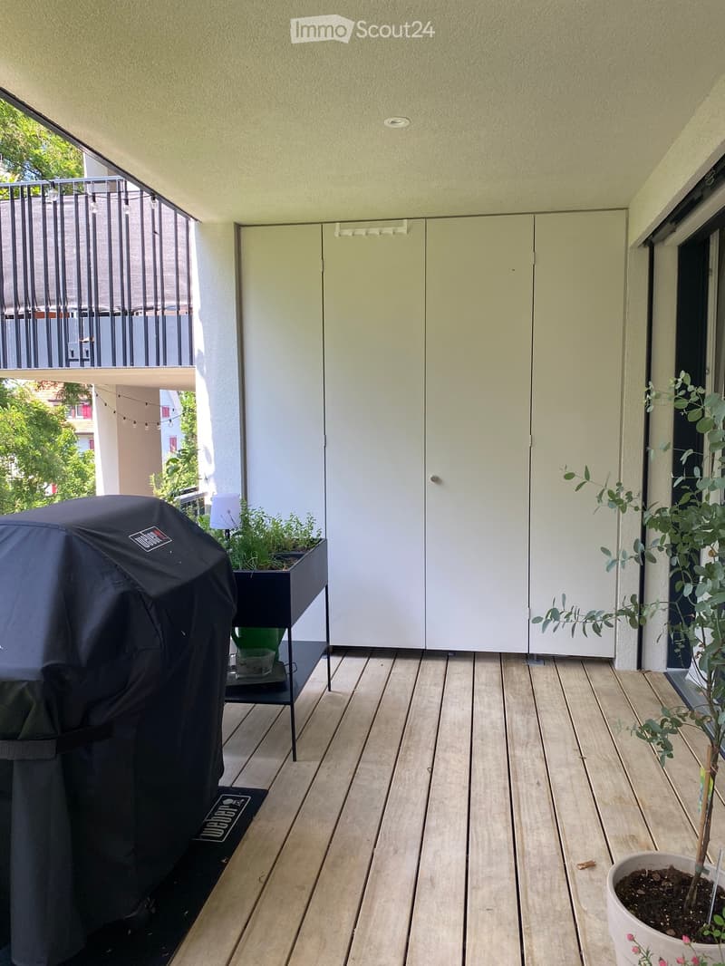 Balcony with wooden decking, grill, potted plants, and a small table.