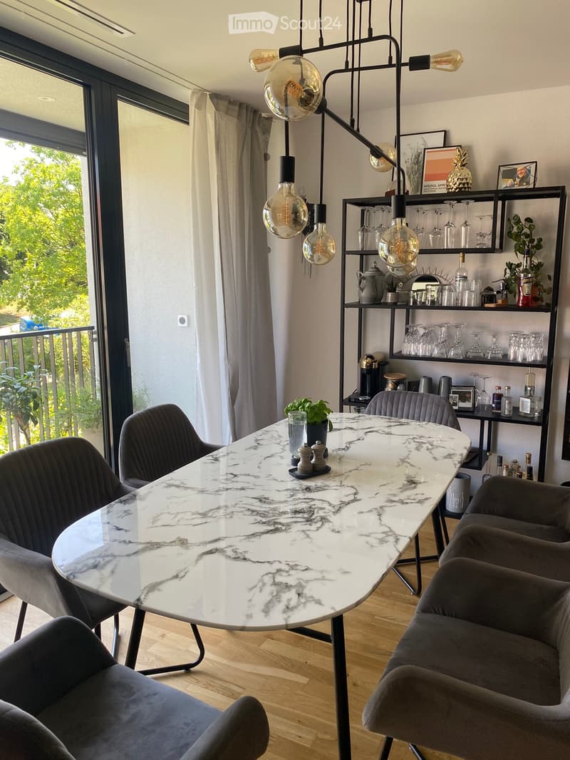 Modern dining area with a marble table, grey chairs, and a shelf with glassware and bottles.