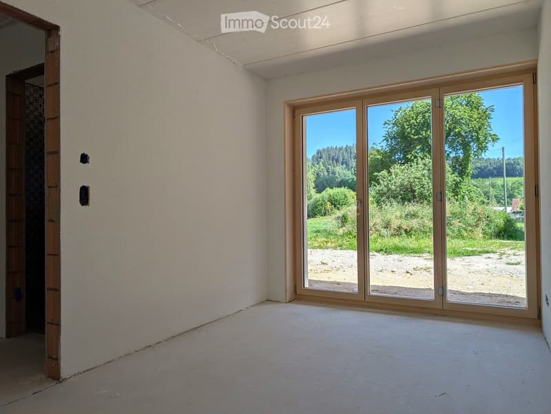 Empty room with white walls, concrete floor, large sliding glass doors leading to an outdoor area with trees and grass.