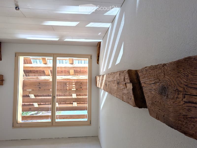 Bright hallway with white walls, wooden ceiling, skylights, and a large wooden beam on the right side. A large window with a view of a wooden deck and pool.
