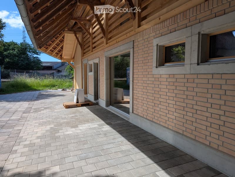Modern building with a mix of brick and wooden exterior, large windows, and a covered wooden entrance area.