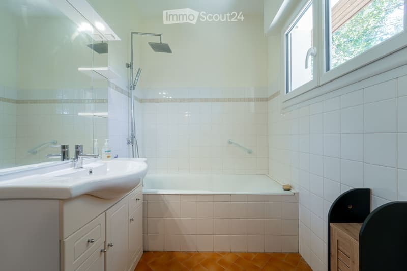 Bathroom with white tiles, a sink, bathtub, showerhead, and a window with a view.