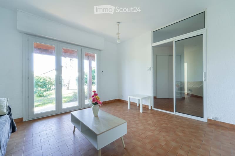 Bright living room with wooden flooring, large sliding glass doors leading to a terrace, a sofa, a coffee table with a vase of flowers, and a small side table.