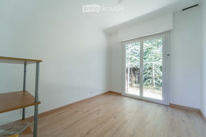 Empty room with light-colored walls, wooden flooring, and a sliding glass door leading to an outdoor area.
