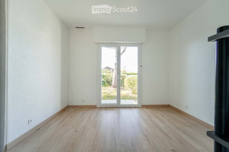 Empty room with light wooden flooring, white walls, and a large glass sliding door leading to an outdoor area.