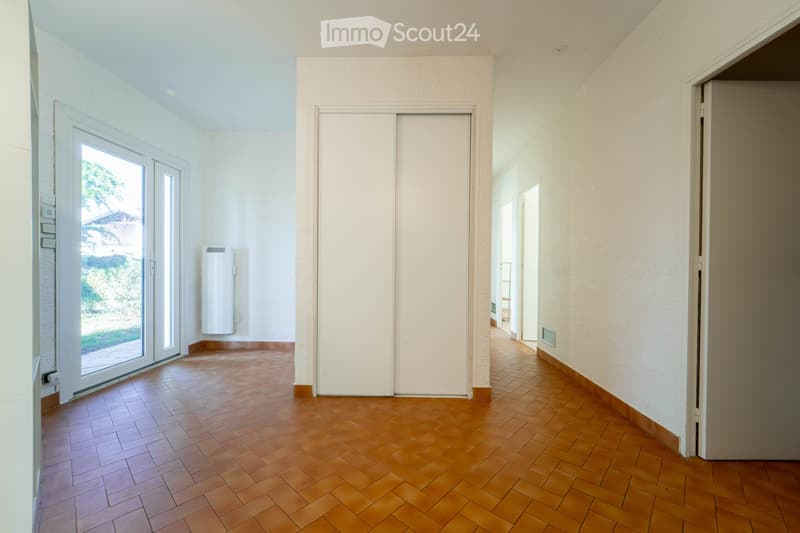 Empty hallway with wooden flooring, white walls, large sliding glass door, radiator, and a closed sliding door leading to another room.