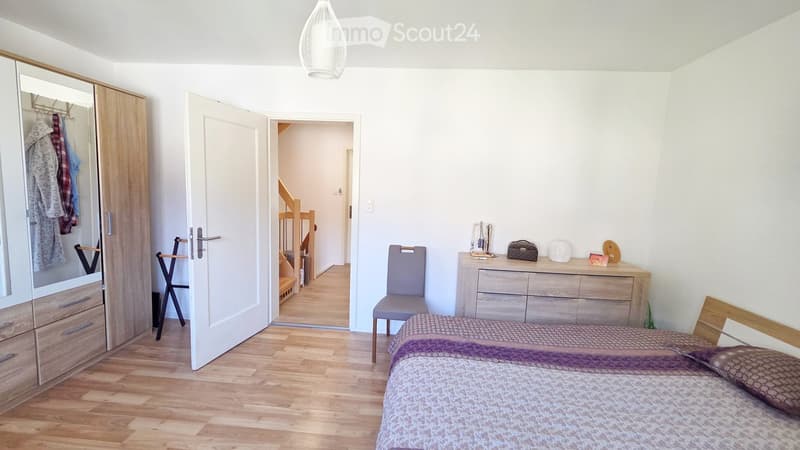 Bedroom, wooden floor, white walls, wooden bed, gray chair, wooden cabinet, closet, open door