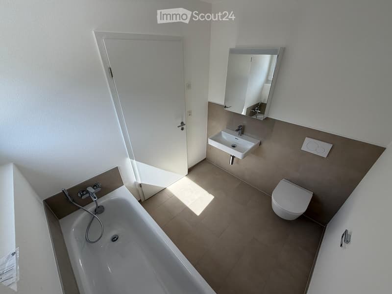 Modern bathroom with a bathtub, toilet, sink, and mirror. Light-colored tiles and neutral walls.