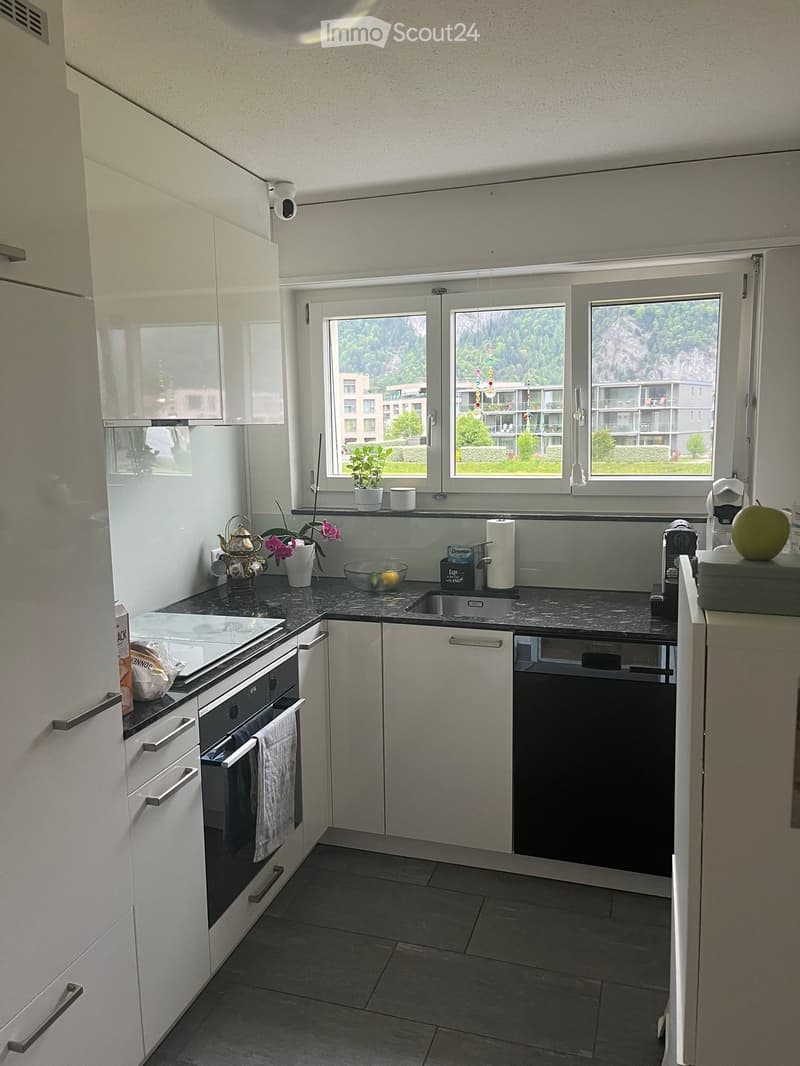 Modern kitchen with white cabinets, dark countertops, and stainless steel appliances. Features an oven, dishwasher, sink, coffee maker, and various kitchen items on the counter.