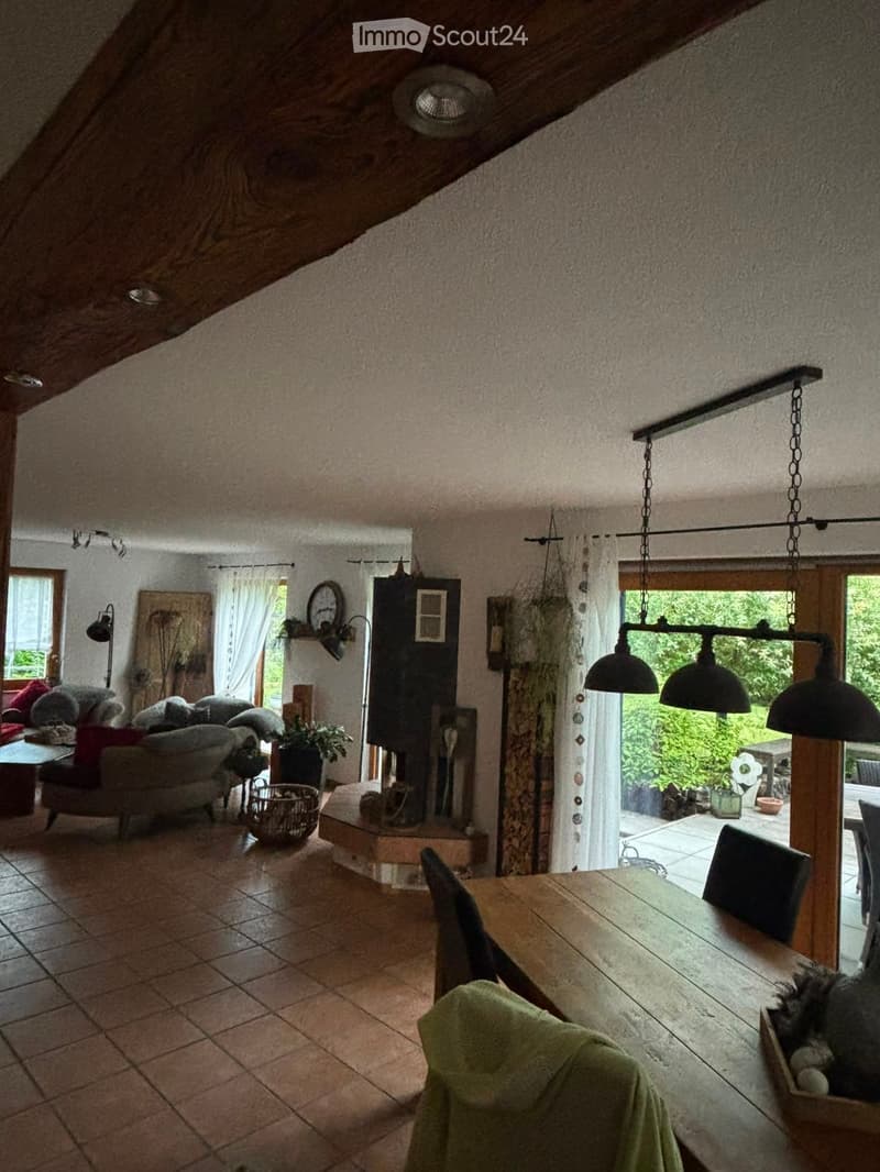 A cozy living and dining area with exposed wooden beams, a fireplace, a sofa, a dining table, and pendant lights.