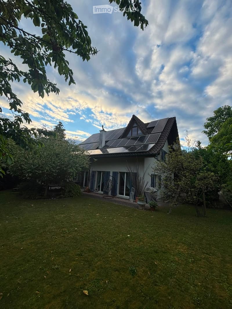 Two-story house with solar panels on the roof, surrounded by a well-maintained lawn and trees.