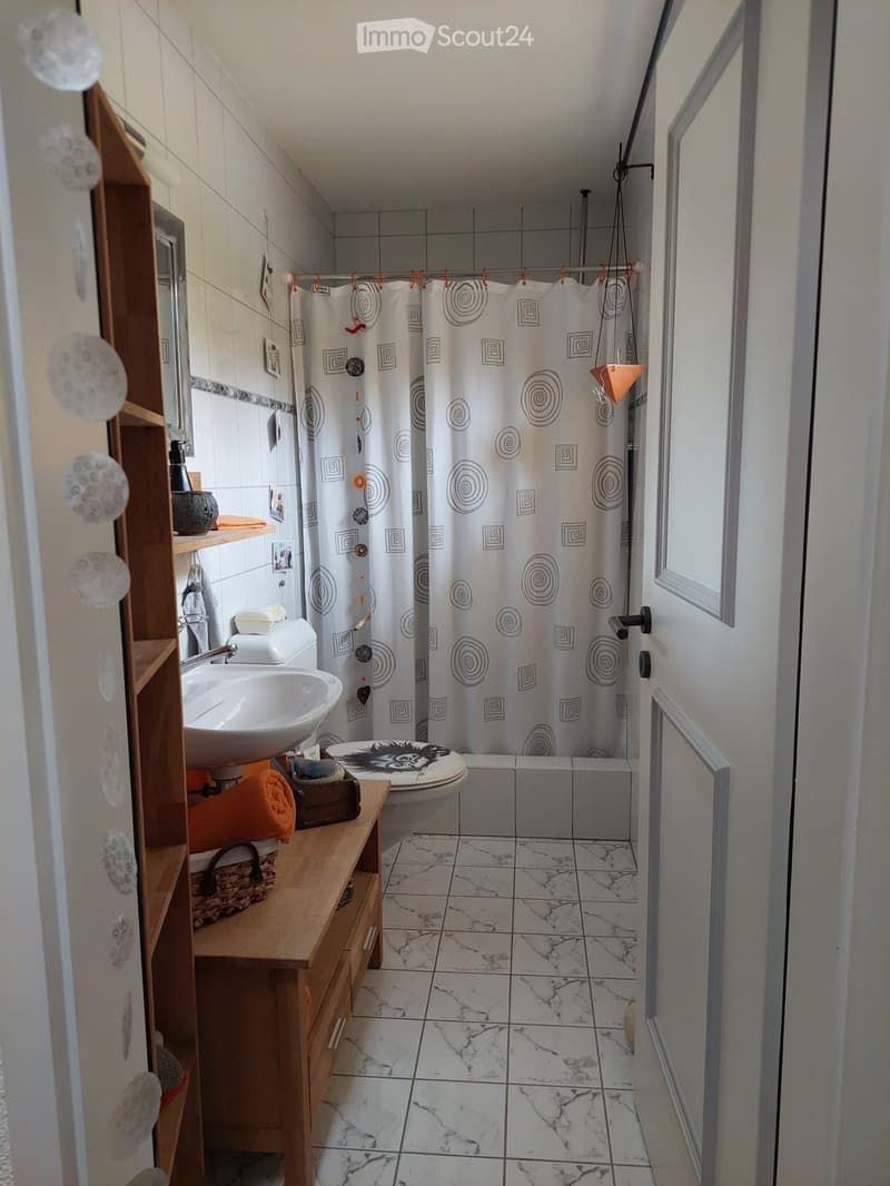 Bathroom with white tiles, marble floor, sink, toilet, bathtub, and wooden shelf with towels and decorative items.