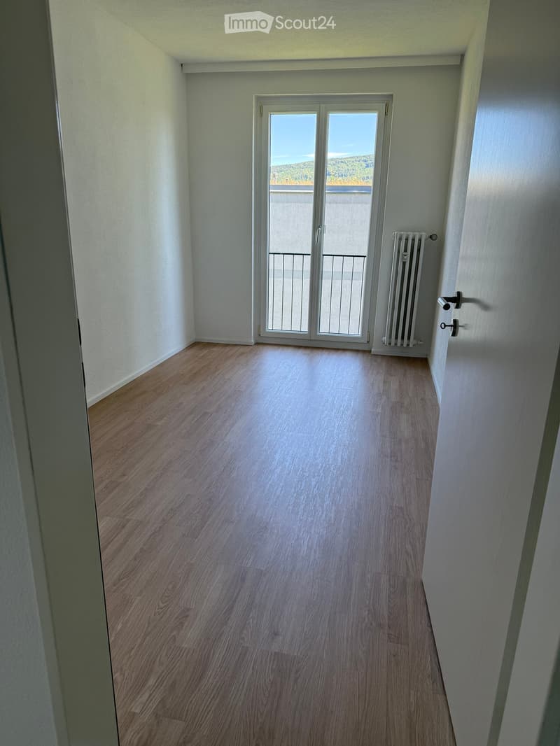 Empty room with wooden flooring, white walls, and a sliding glass door leading to a balcony with a view.