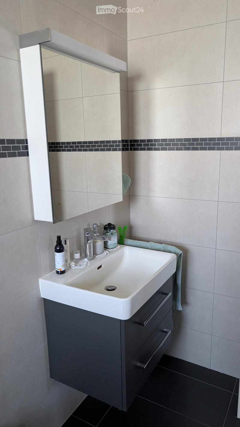 Modern bathroom with a white sink, dark grey cabinet, mirror, and various toiletries on the sink counter.