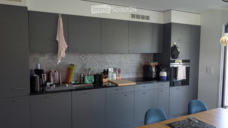 Modern kitchen with grey cabinets, stainless steel appliances, and a wooden dining table with blue chairs.