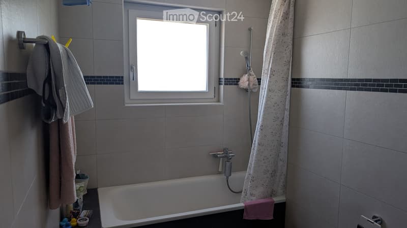 Bathroom with a bathtub, shower, window, and towels hanging on the wall.