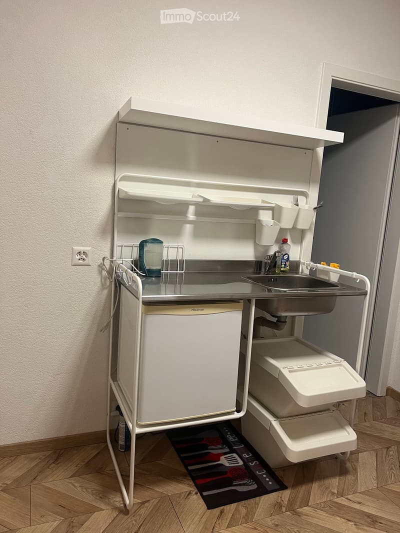 Compact kitchen with a refrigerator, sink, faucet, and various small appliances and utensils neatly arranged on shelves and counters.