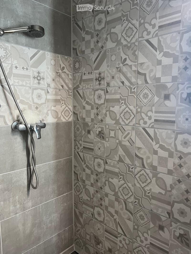 Shower area with grey and black patterned tiles, chrome showerhead, and faucet.