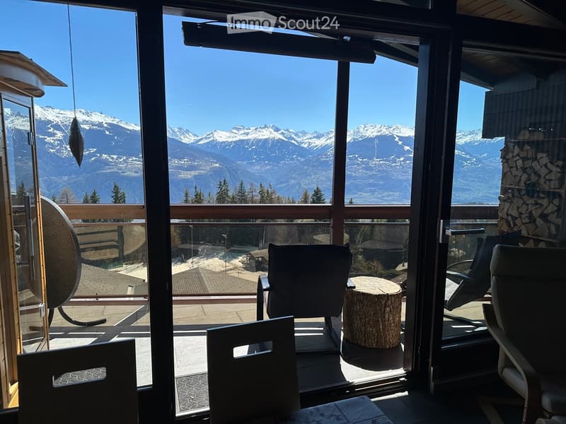 Balcony with panoramic mountain view, featuring several chairs and a small table.