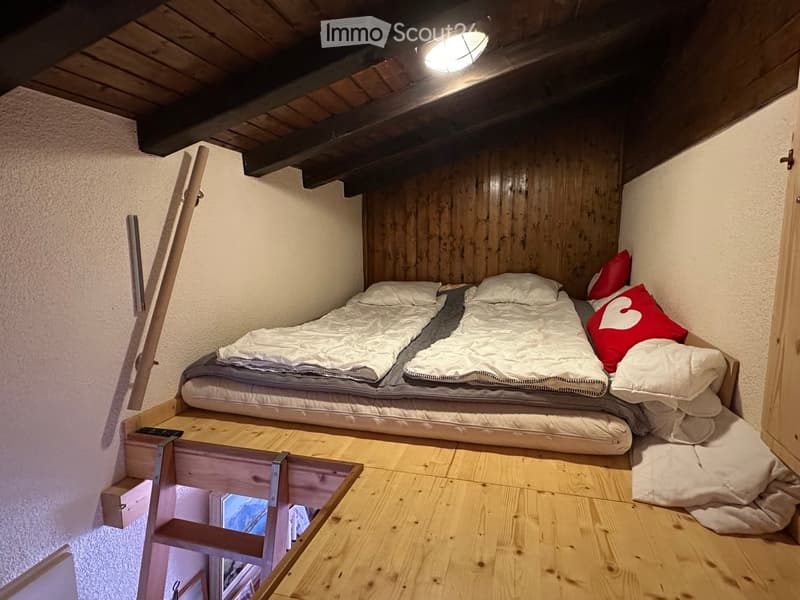 Cozy attic bedroom with wooden walls and slanted ceilings, featuring a built-in bed platform with pillows and blankets.