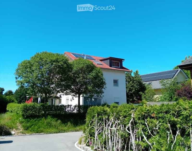 Two-story house with red-tiled roof, white walls, solar panels, surrounded by greenery and a curved driveway.