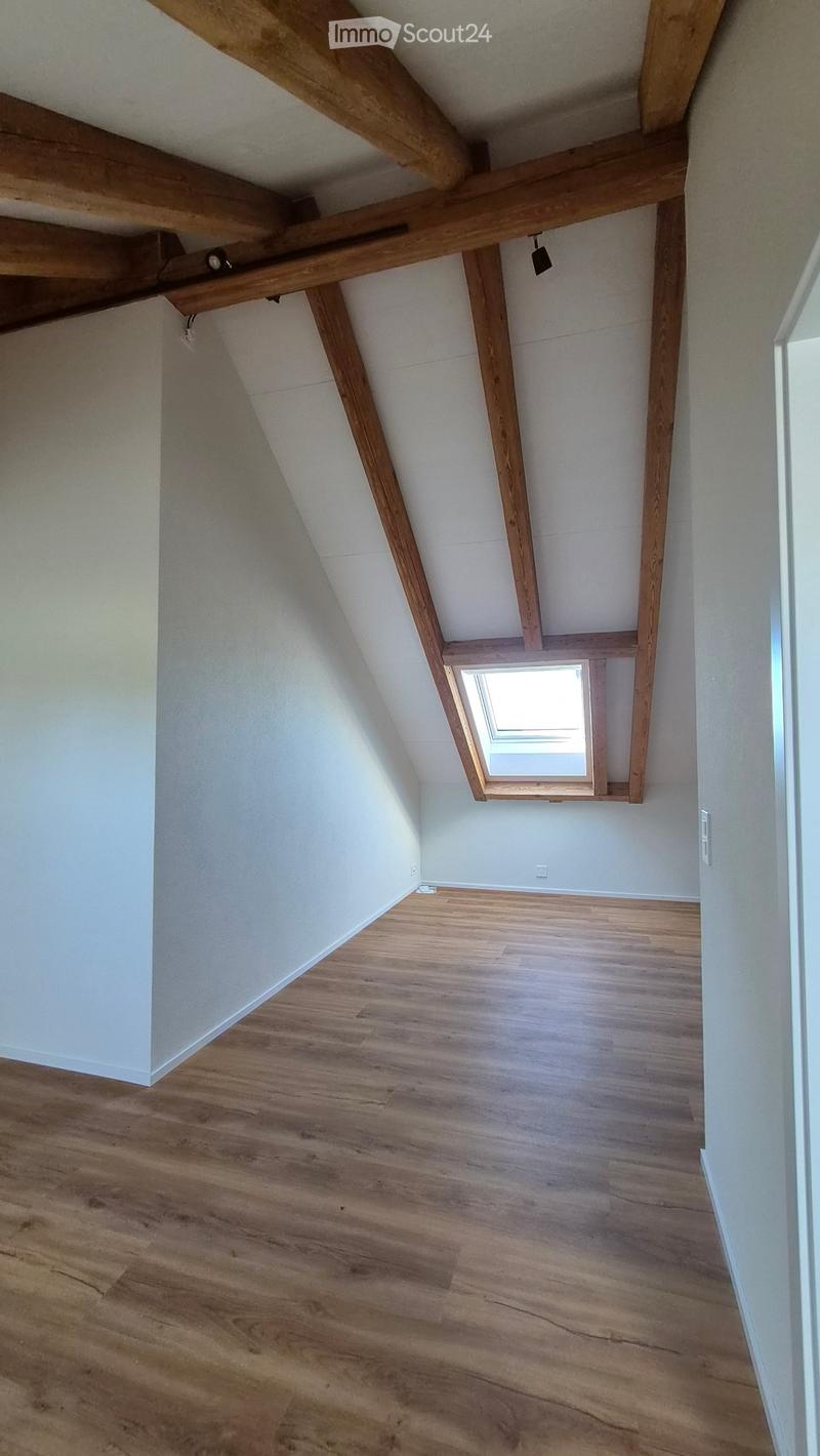 Empty attic space with wooden beams, wooden flooring, and a skylight window letting in natural light.