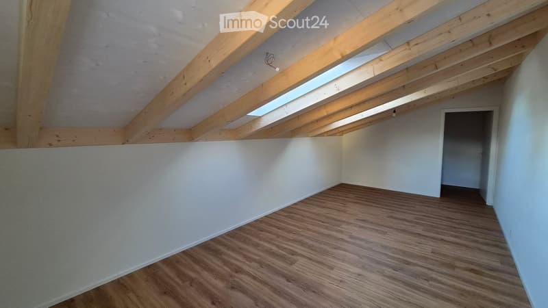 Empty attic space with wooden floor, white walls, exposed wooden beams, and skylight windows.