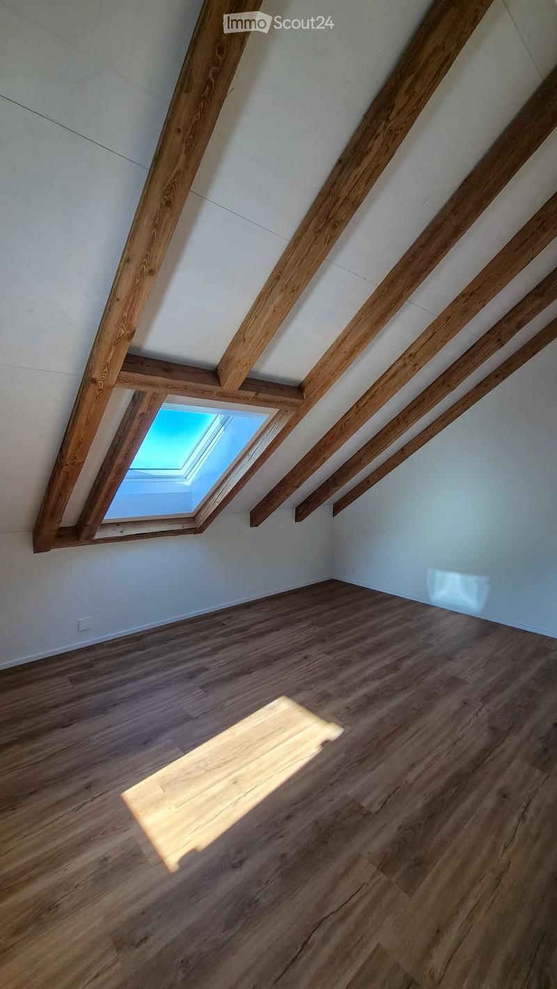Empty attic space with wooden beams, wooden flooring, and a skylight window allowing natural light to enter.