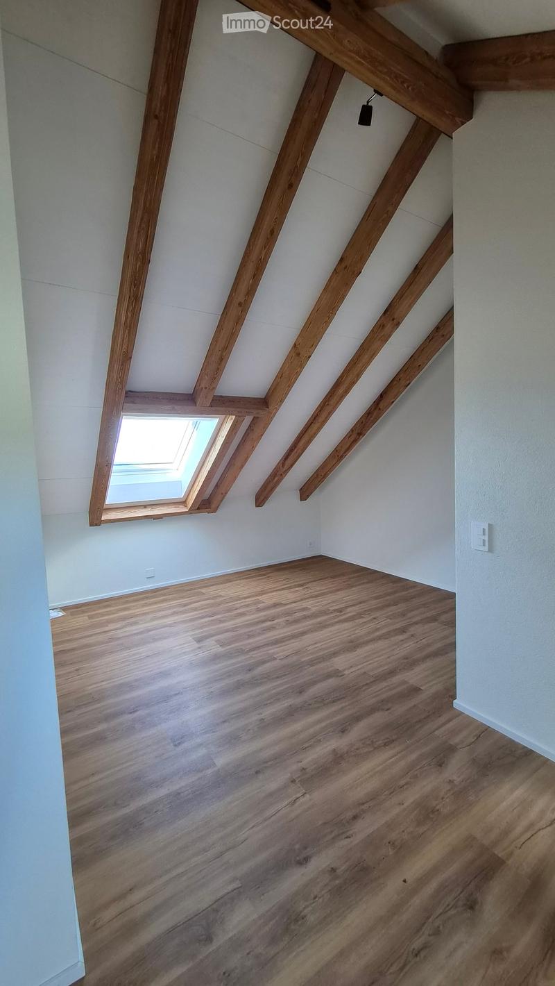 Empty attic space with wooden beams, light-colored wooden flooring, and a skylight window letting in natural light.