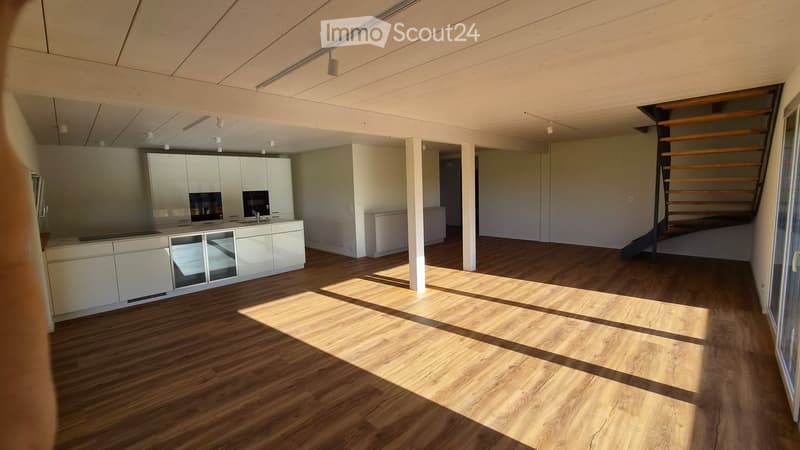 Open-plan kitchen and living area with light-colored wooden flooring, white kitchen cabinets, and a staircase leading to an upper level.