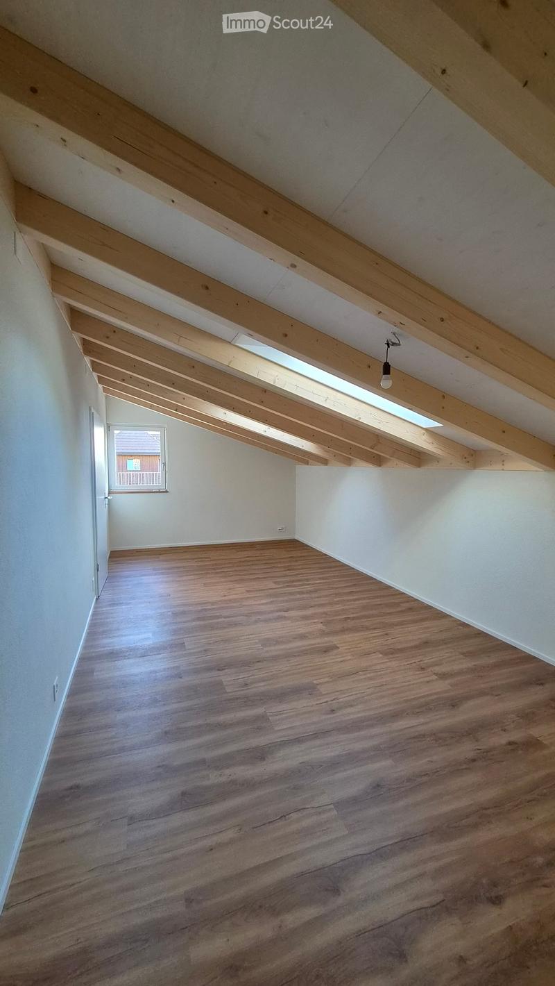 Empty attic space with wooden beams, skylight, and wooden flooring.