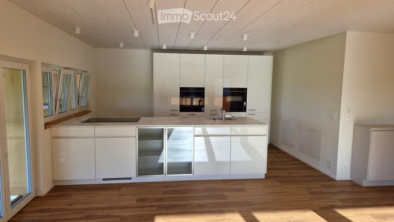 Modern kitchen with white cabinets, a central island, and a wooden floor. Features include a sink, faucet, and built-in oven.
