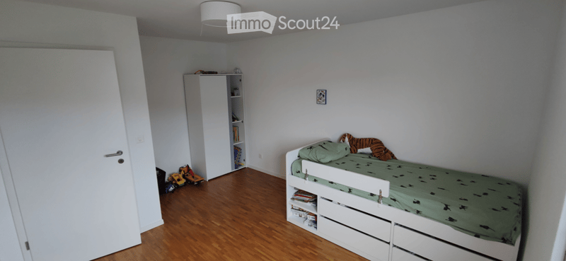 A small bedroom with a single bed, green bedding, a white wardrobe, and a few toys on the floor.
