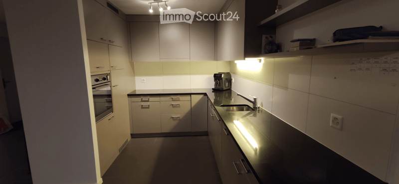 Modern kitchen with light-colored cabinets, black countertops, built-in oven, sink, and coffee maker. Features recessed lighting and a sleek design.